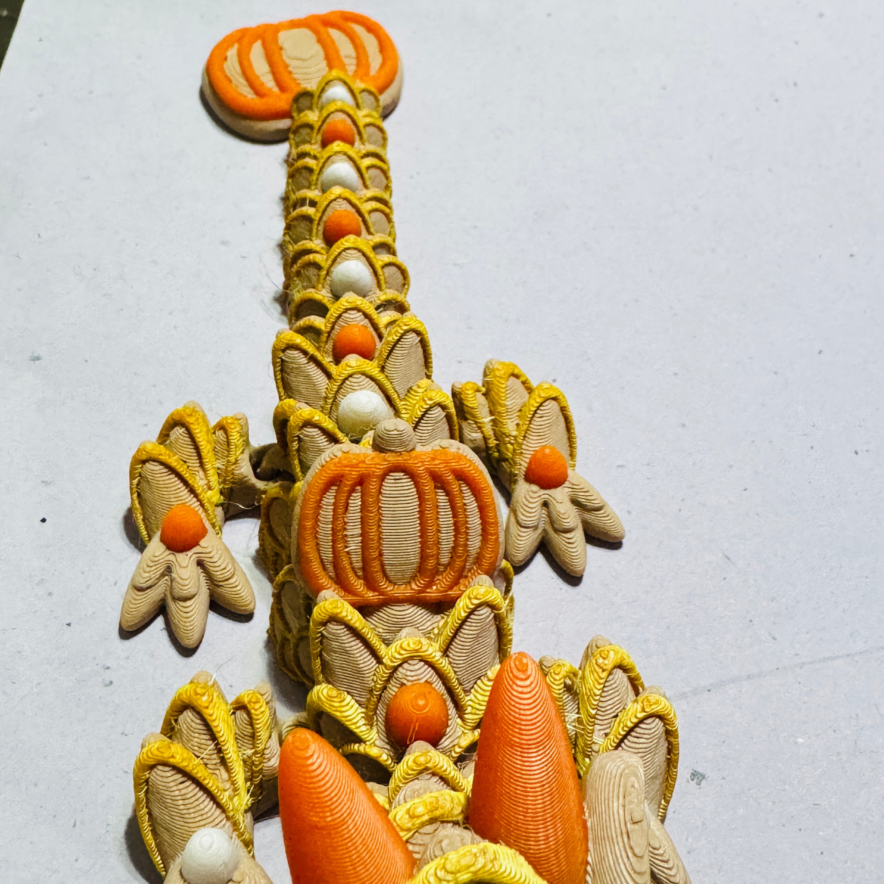 Close-up of articulated dragon body showing smooth 3D printed layers and joint movement in pumpkin-themed colors